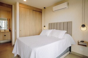 A hotel room with a bed, a bedside table, a nightstand, an air conditioning unit, and a mirror. - Modern Oceanfront Loft and Beach | Santa Marta (Santa Marta)