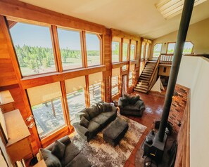 A spacious living area with large windows, a fireplace, and a staircase leading to an upper level. - Sunrise Ridge•SwimSpa•Pikes Peak Views • Sleeps 10 (Divide)