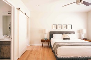 A bedroom with a bed, bedside tables, a nightstand, a ceiling fan, and framed artwork on the wall.