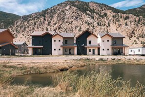 A row of modern houses with a mountain backdrop, a small pond, and a clear sky.
