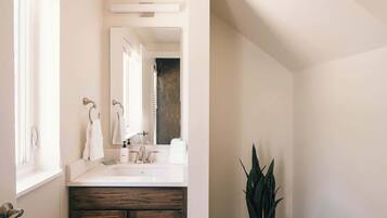 A bathroom with a white sink, a mirror, a wooden cabinet, and a potted plant.