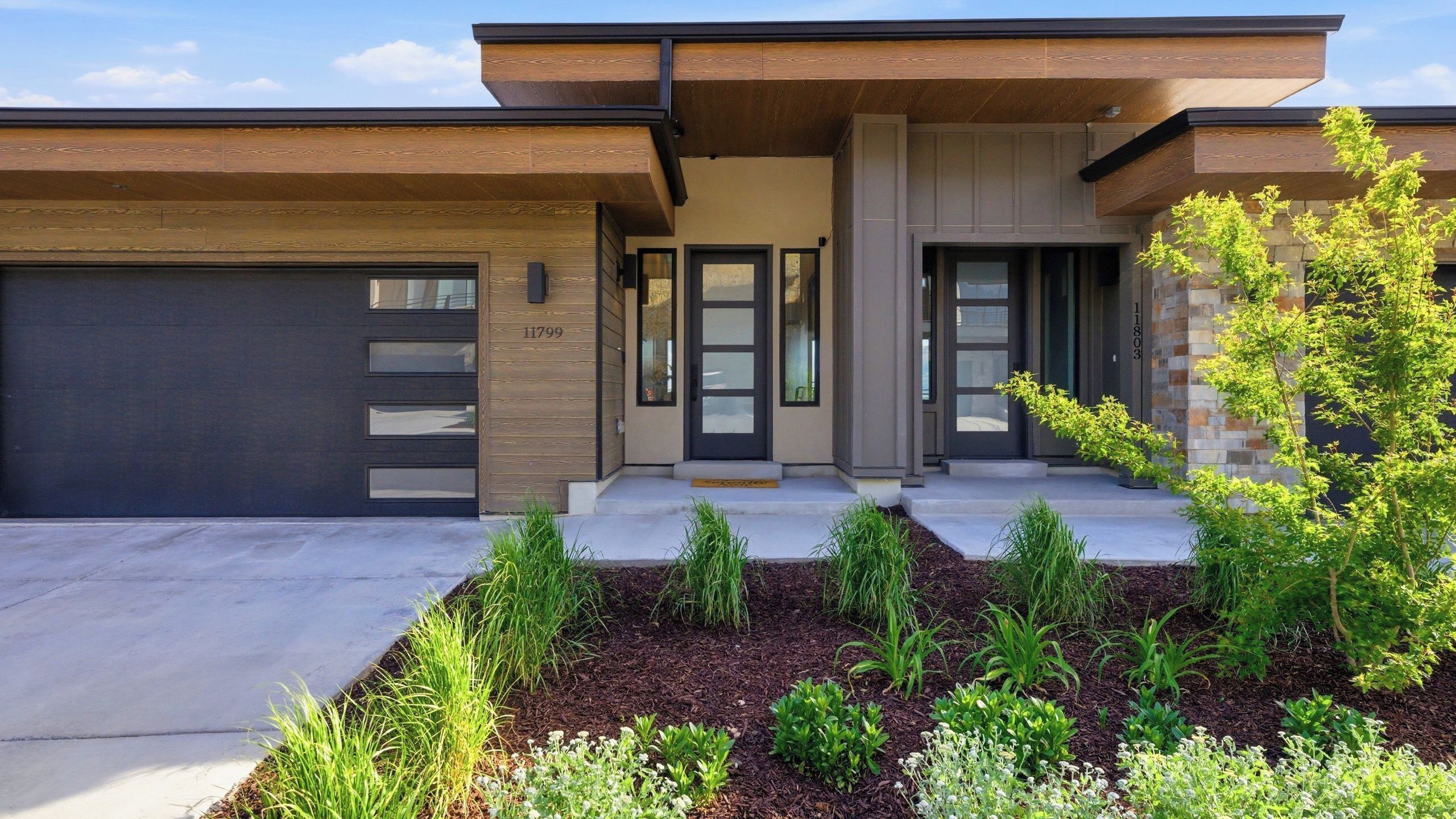 A modern two-story house with a garage, a front porch, and a landscaped garden.