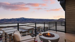 Ein Balkon mit Feuerstelle, Sitzgelegenheiten und Blick auf Berge und ein Gewässer.