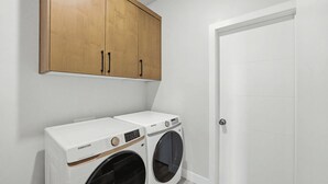 Un lavadero con dos lavadoras Samsung blancas, un armario de madera arriba y una puerta blanca.