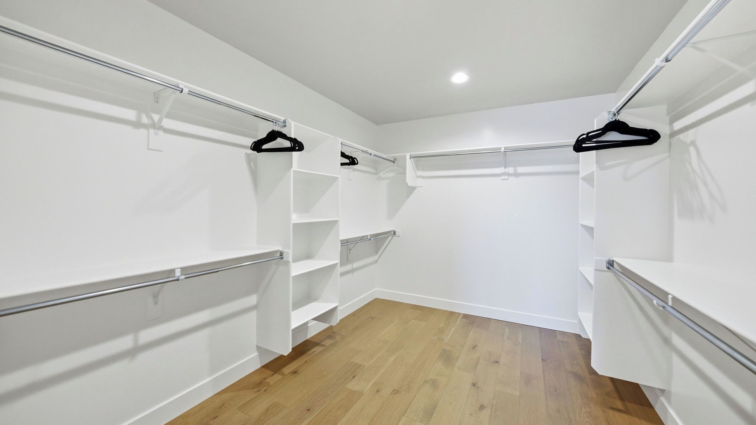 A walk-in closet with white walls, wooden flooring, and multiple shelves and hangers.