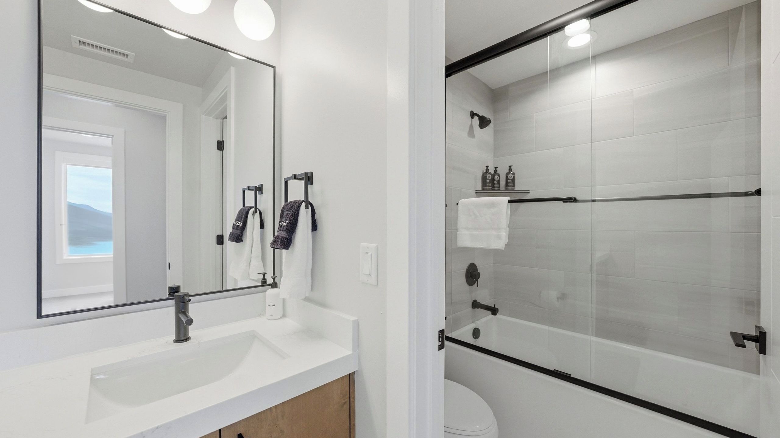 A modern bathroom with a large mirror, a sink, and a glass-enclosed shower area.