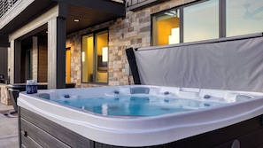 Ein Whirlpool mit Steinwand im Hintergrund, einer überdachten Terrasse und einem Fenster mit Blick ins Innere.
