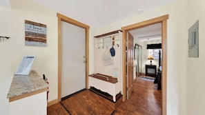 A hallway with wooden flooring, a door with a wooden frame, a coat rack with hats, and a small table with a lamp.