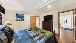 A bedroom with a bed, a dresser, a TV, and a door leading to another room.