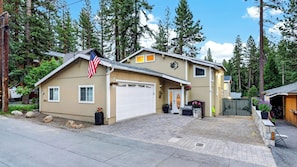 A two-story house with a garage, a front porch with potted plants, and a flag.