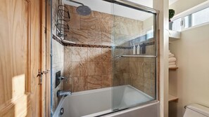 A glass-enclosed shower with a bathtub, tiled walls, and a wooden door.