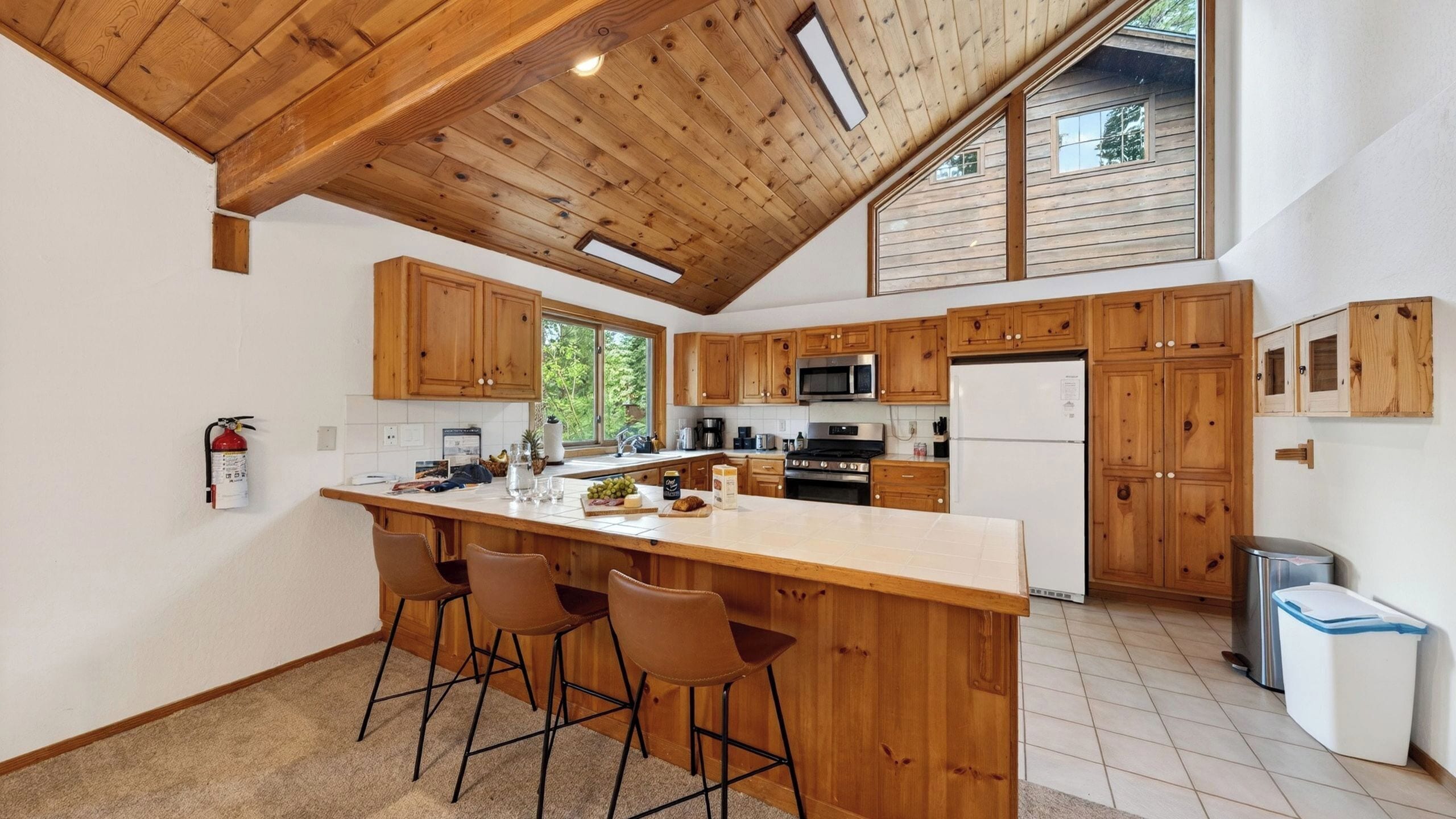 A kitchen with wooden cabinets, a central island with bar stools, a stainless steel refrigerator, and a microwave.