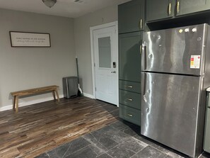 Una cocina con un refrigerador de acero inoxidable, un banco de madera, un bote de basura y una puerta con ventana.