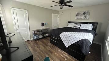 Une chambre à coucher comprenant un lit, un bureau, une chaise, un ventilateur de plafond et une lampe fixée au mur.