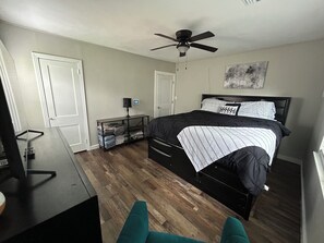 Un dormitorio con cama, escritorio, silla, ventilador de techo y lámpara de pared.