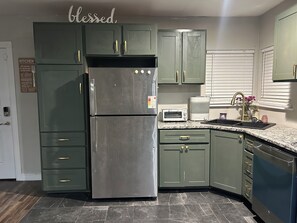 Una cocina con armarios verdes, un refrigerador de acero inoxidable, un tostador y un lavamanos.