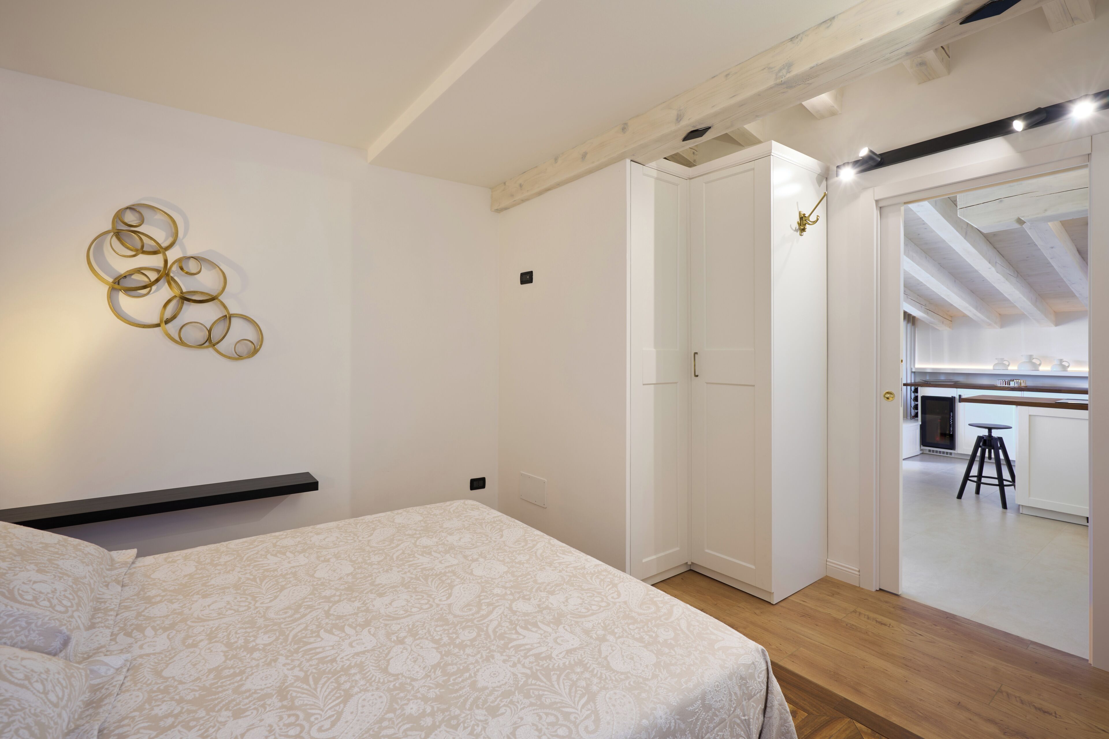 Un dormitorio con cama, lámpara de pared y puerta que da a una zona de cocina.