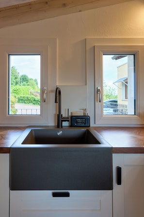 A kitchen with a modern sink, two windows, and a view of greenery outside.