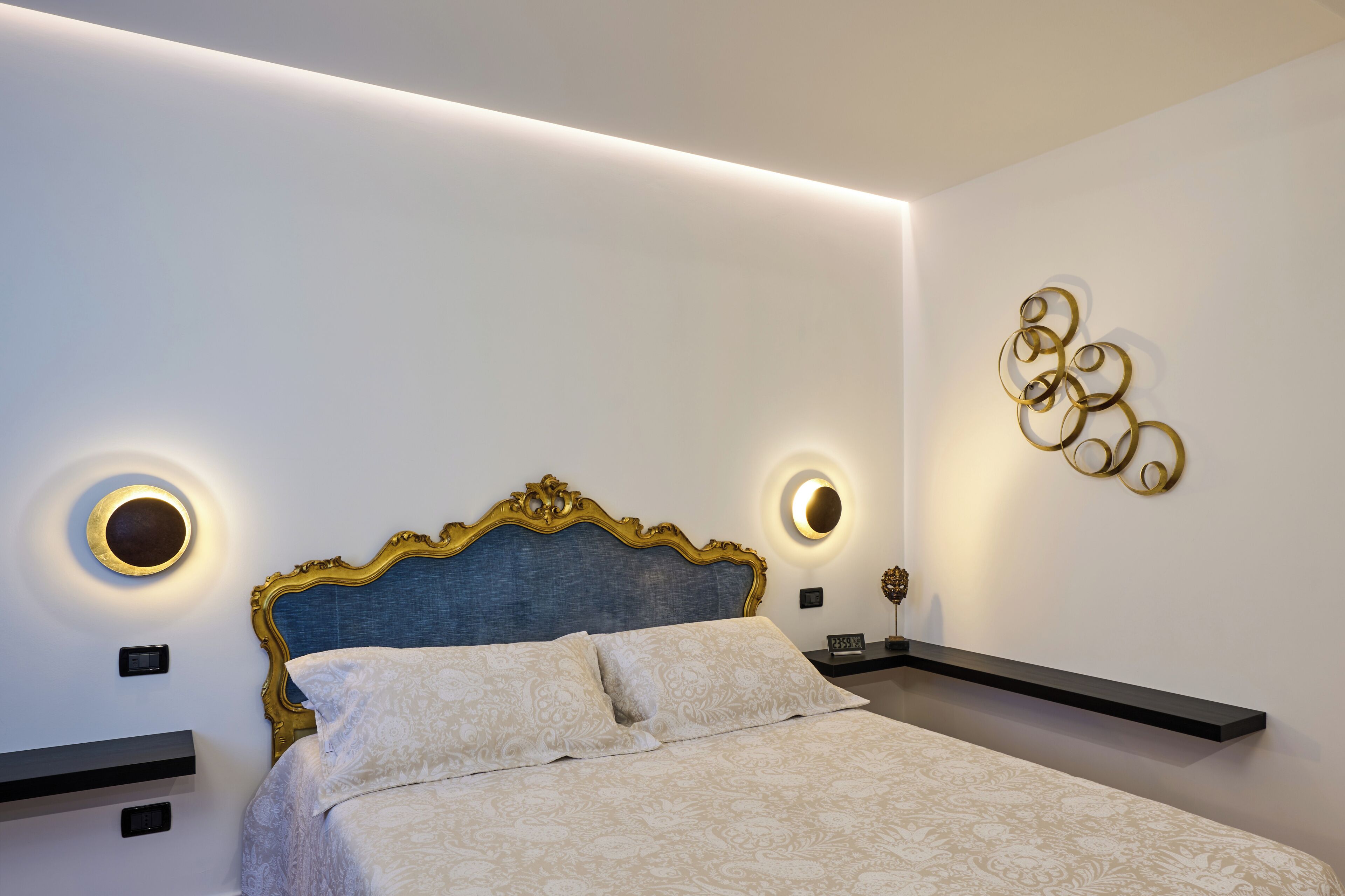 A bedroom with a bed, bedside tables, wall sconces, and a decorative wall piece.