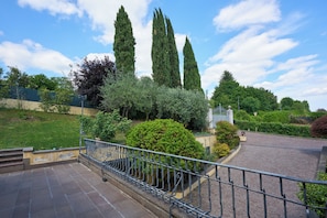 A paved area with a metal railing, a statue, and tall trees.