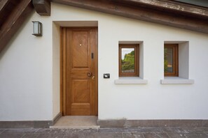 A wooden door with a small window above it, a wall-mounted light, and a small window on the right.