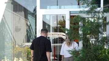 A hotel entrance with a modern design, a sign reading 'DORA BEYTEPE', and a person pulling a suitcase.