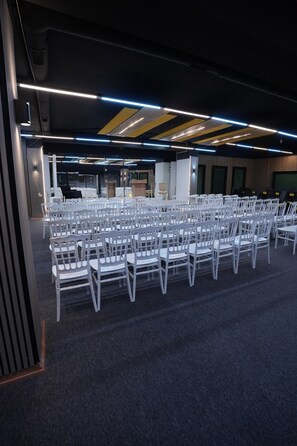 A conference room with rows of white chairs, a stage with a podium, and a carpeted floor. - DORA BEYTEPE HOTEL (Ankara)