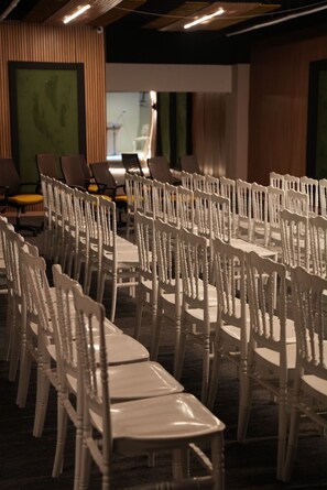 Filas de sillas blancas dispuestas en un salón de conferencias con un escenario y un piano al fondo.