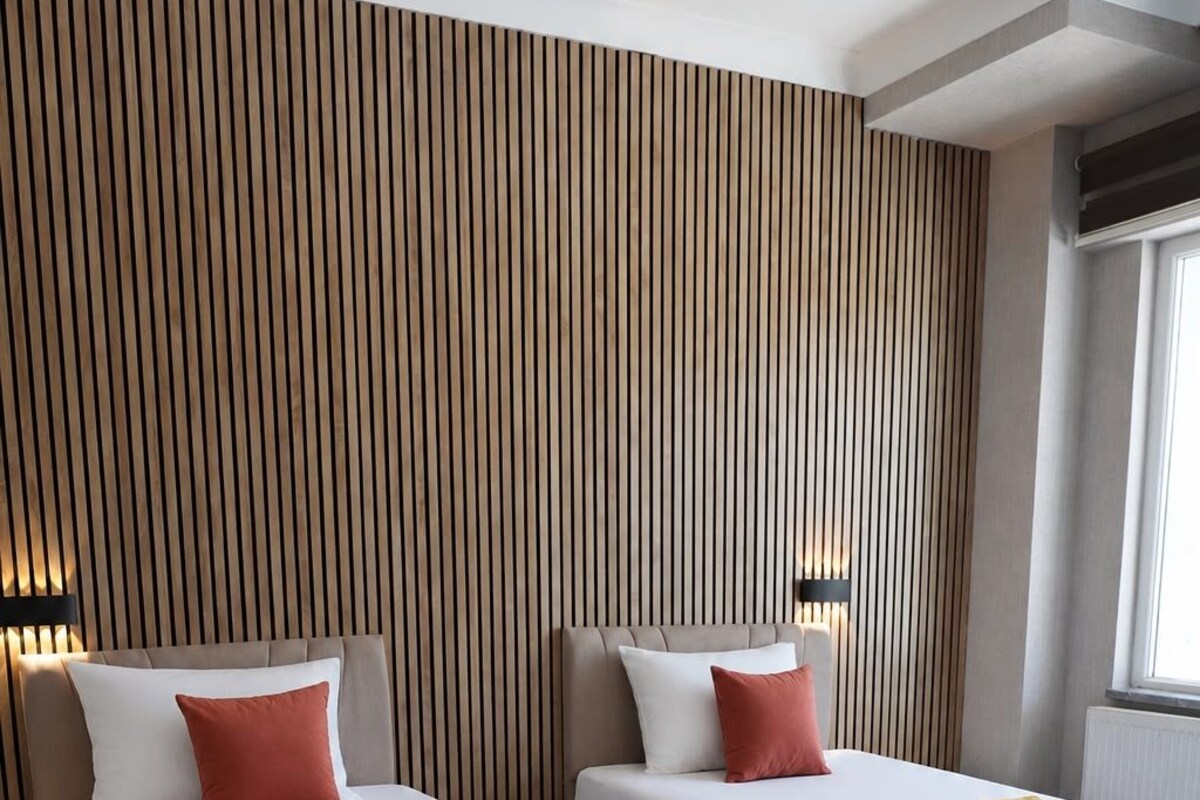 Habitación de hotel con dos camas, cada una con cubrecama rojo y blanco, una toalla amarilla y un panel de madera con listones.