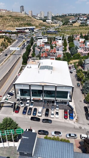 A multi-story building with a flat roof, surrounded by parked cars and a road.