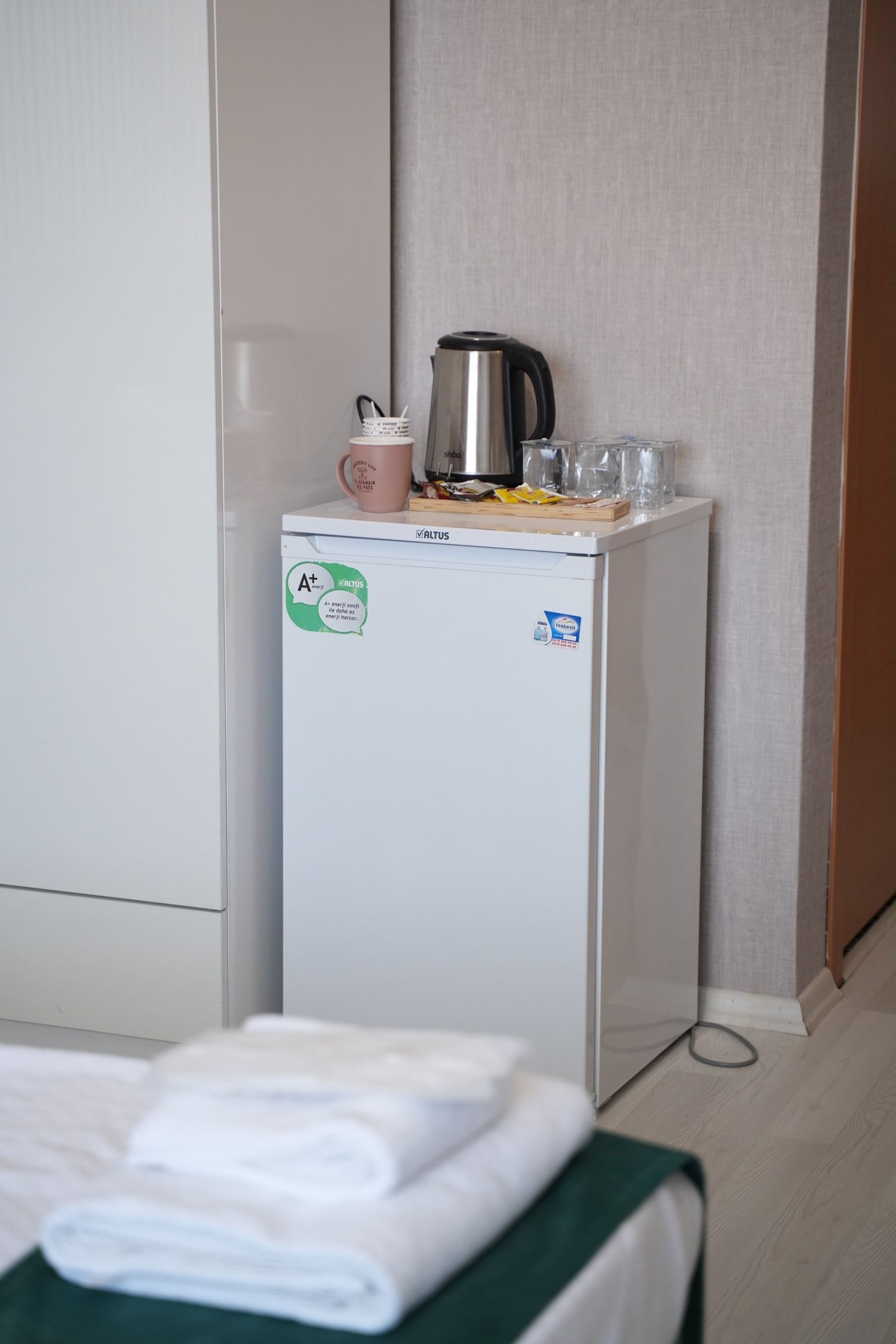 A compact refrigerator with a sticker indicating energy efficiency, a kettle, a mug, and a glass on top.