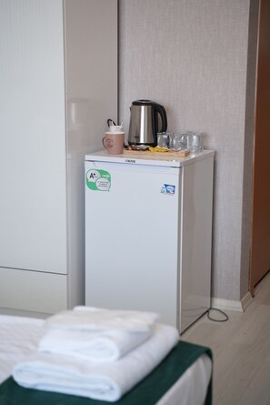 A compact refrigerator with a sticker indicating energy efficiency, a kettle, a mug, and a glass on top. - DORA BEYTEPE HOTEL (Ankara)