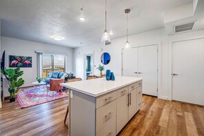 A modern kitchen with white cabinets, a central island, pendant lights, and a view to the outside.