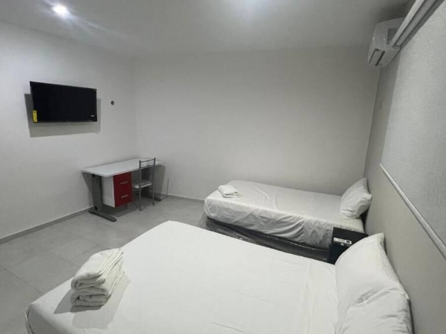 Una habitación con dos camas, un escritorio, una silla, un televisor y un armario rojo.