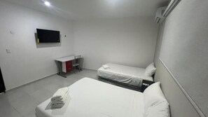 A room with two beds, a desk, a chair, a TV, and a red cabinet. - Departamentos 597 (Mérida)