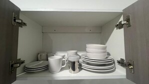 A storage space with a toilet, a stack of plates, a mug, and a cup.