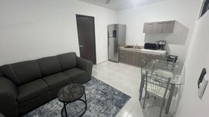 A compact living space with a sofa, a small round table, a kitchen area with a refrigerator, microwave, and cabinets. - Departamentos 597 (Mérida)