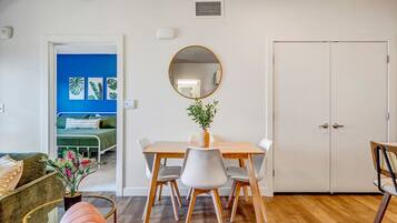 A dining area with a wooden table and chairs, a round mirror, and a potted plant.
