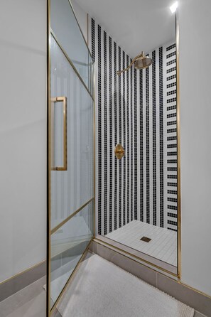 Ein modernes Badezimmer mit einer Duschkabine aus Glas, einem goldfarbenen Duschkopf und einer Wand mit gemusterten Fliesen.