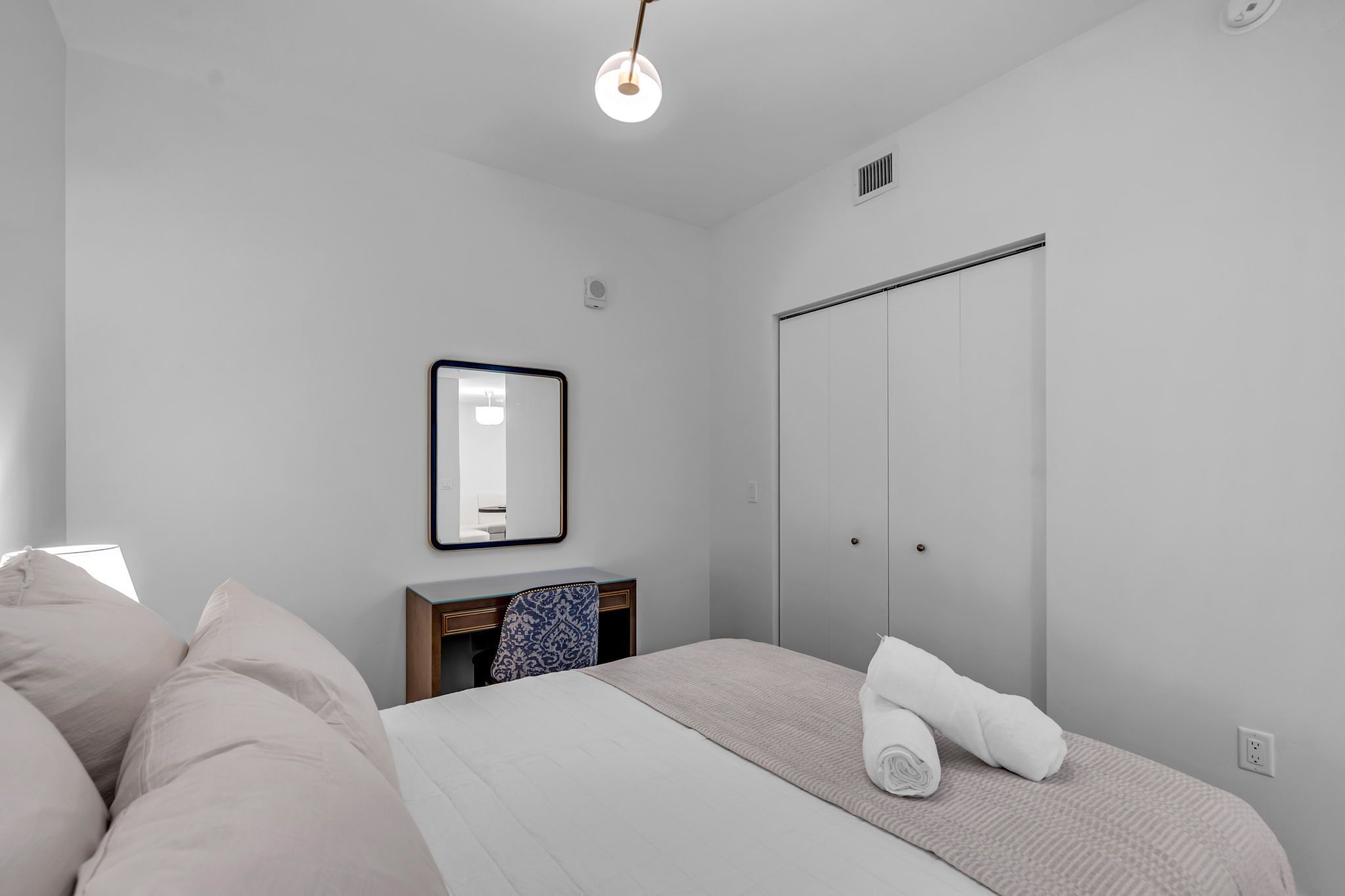 Une chambre d’hôtel minimaliste comprenant un lit, un bureau, une chaise, une armoire et un miroir.