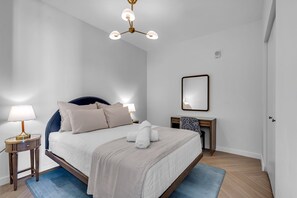 Een keurig opgemaakt slaapkamer met een bed, nachtlampjes, een bureau en een spiegel.