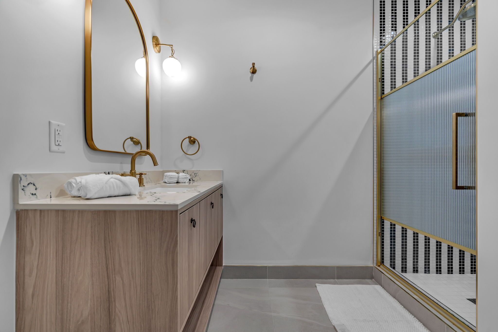 Een moderne badkamer met een houten wastafelmeubel, een grote spiegel en een douchecabine.