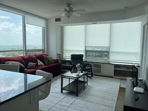 Una sala de estar moderna con un sofá rojo, una silla negra, una mesa de centro de vidrio y vistas de la ciudad a través de amplios ventanales.