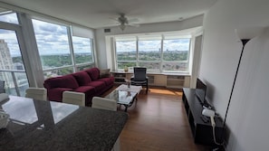 Una sala de estar moderna con un sofá, una mesa de centro, un televisor y grandes ventanales con vistas a la ciudad.