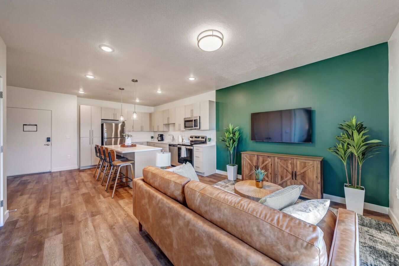 A modern kitchen with white cabinets, a central island, and a dining area with a brown leather sofa and a round coffee table.