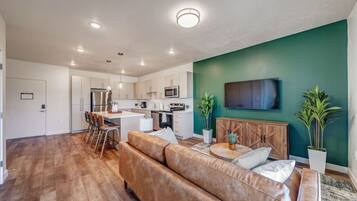 A modern kitchen with white cabinets, a central island, and a dining area with a brown leather sofa and a round coffee table.