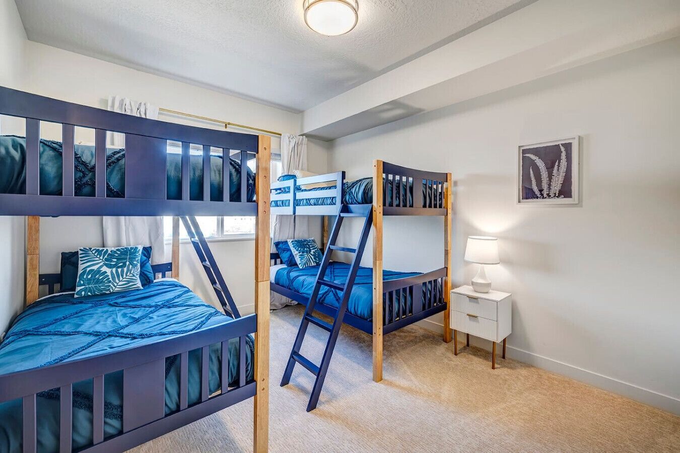 A room with bunk beds, a small bedside table, and a framed picture on the wall.