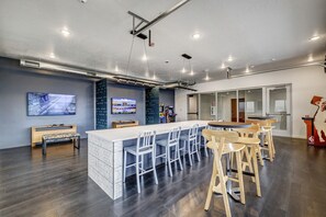 Un grand espace bar doté d’un long comptoir et de nombreux tabourets, d’un banc et d’un téléviseur fixé au mur.