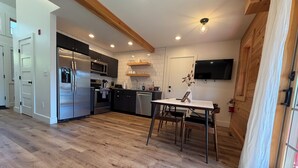 A modern kitchen with a stainless steel refrigerator, microwave, and oven, wooden flooring, and a dining area with a table and chairs.