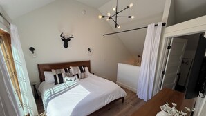 A bedroom with a wooden bed, a mounted deer head, a chandelier, and a white vase with flowers.